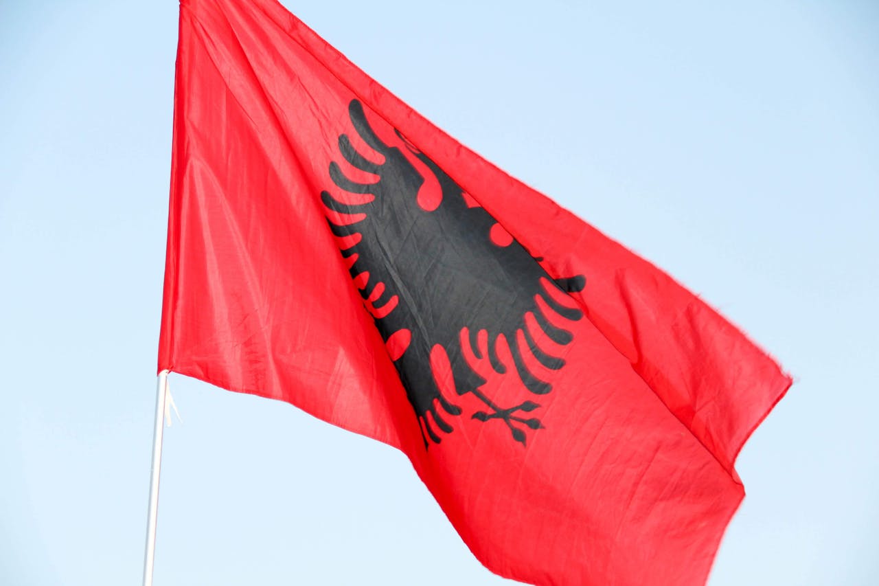 services-01 A vibrant red flag with a black double-headed eagle, symbolizing Albania, waving proudly against a clear blue sky.